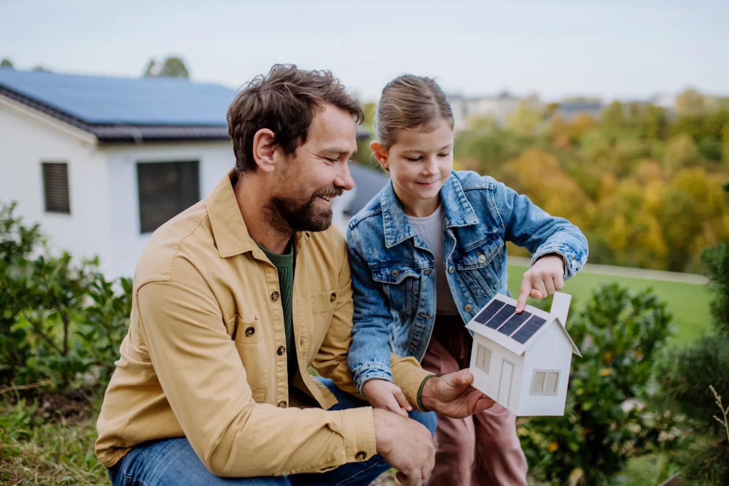 Vader en dochter bekijken een modelwoning met zonnepanelen, passend bij advies over het verzekeren van huis en gezin.