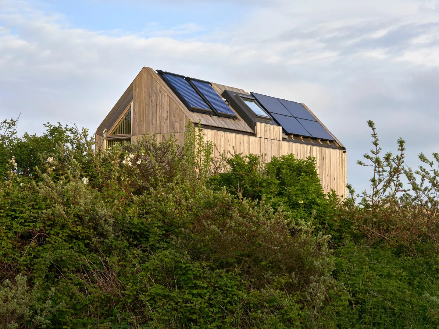 Houten woning met zonnepanelen en zonnecollectoren op het dak, omringd door groen.