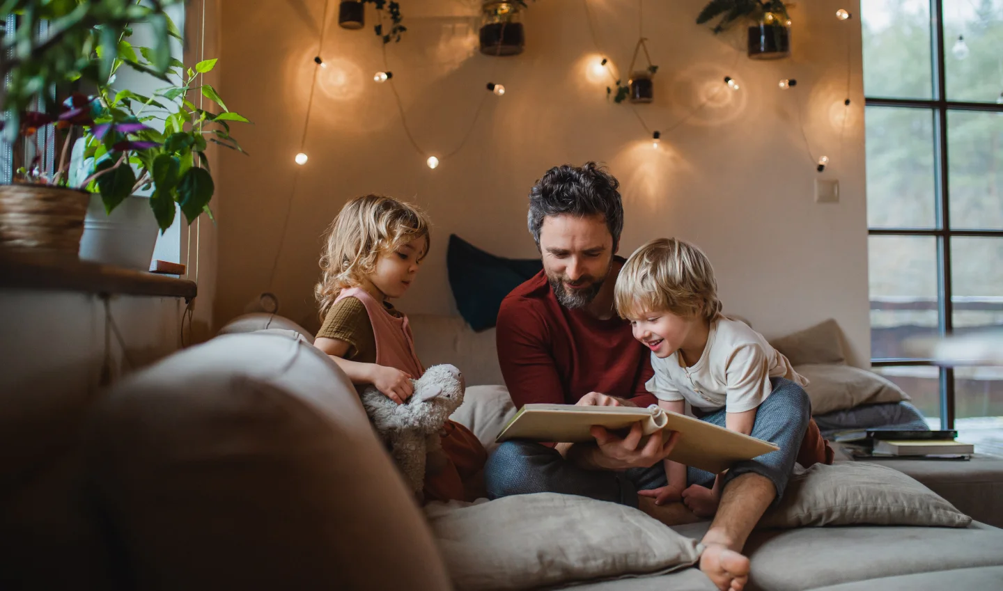 Een vader met twee kleine kinderen die binnenshuis in huis uitrusten en naar een fotoalbum kijken
