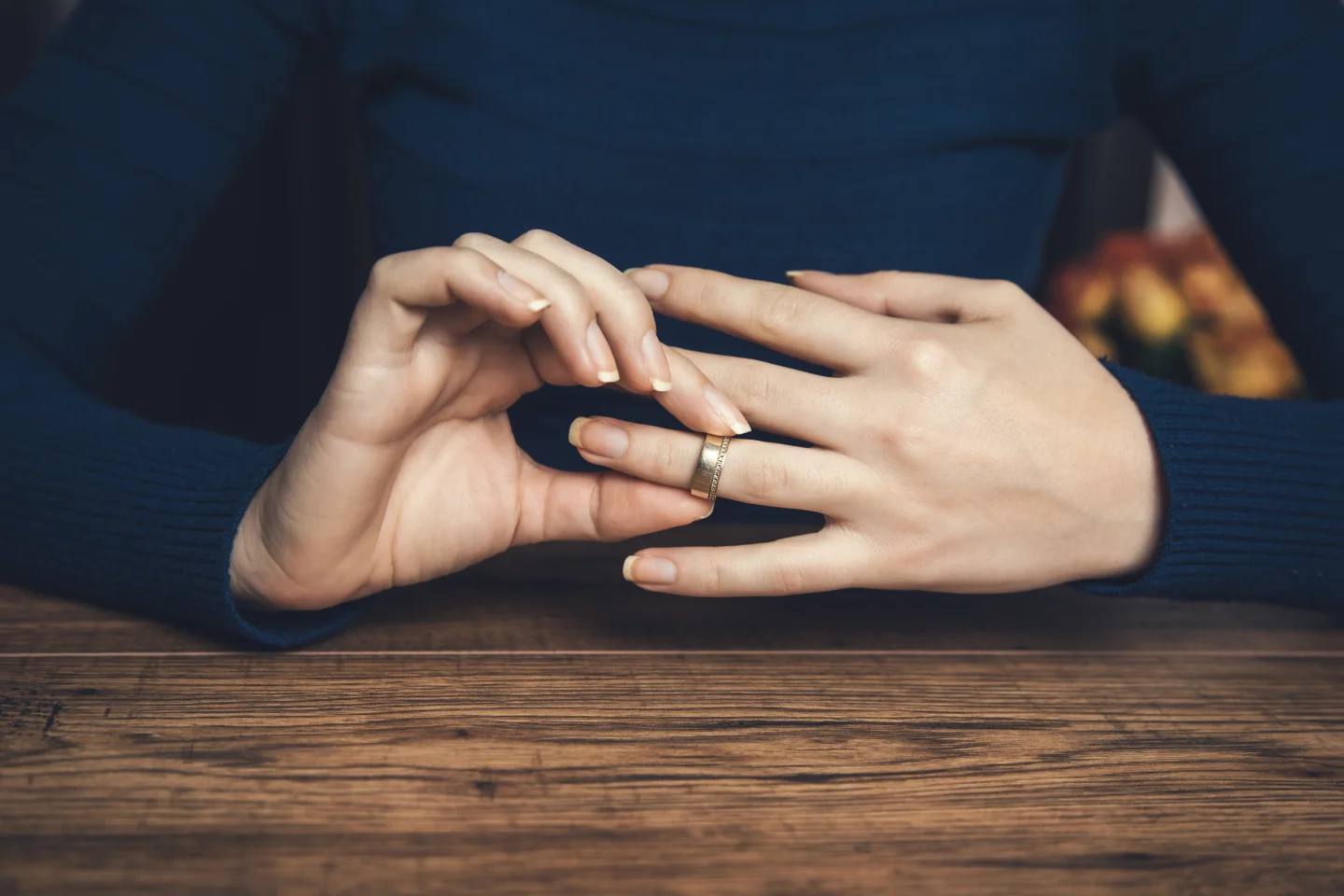 Een vrouw doet haar trouwring af op een houten tafel.