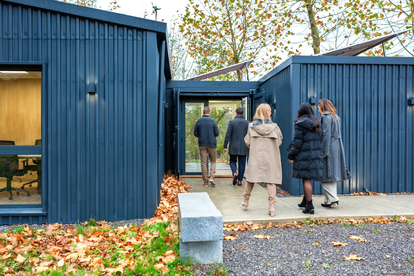 Groep mensen bezichtigt moderne woning met blauwe gevel en grote ramen in herfstomgeving