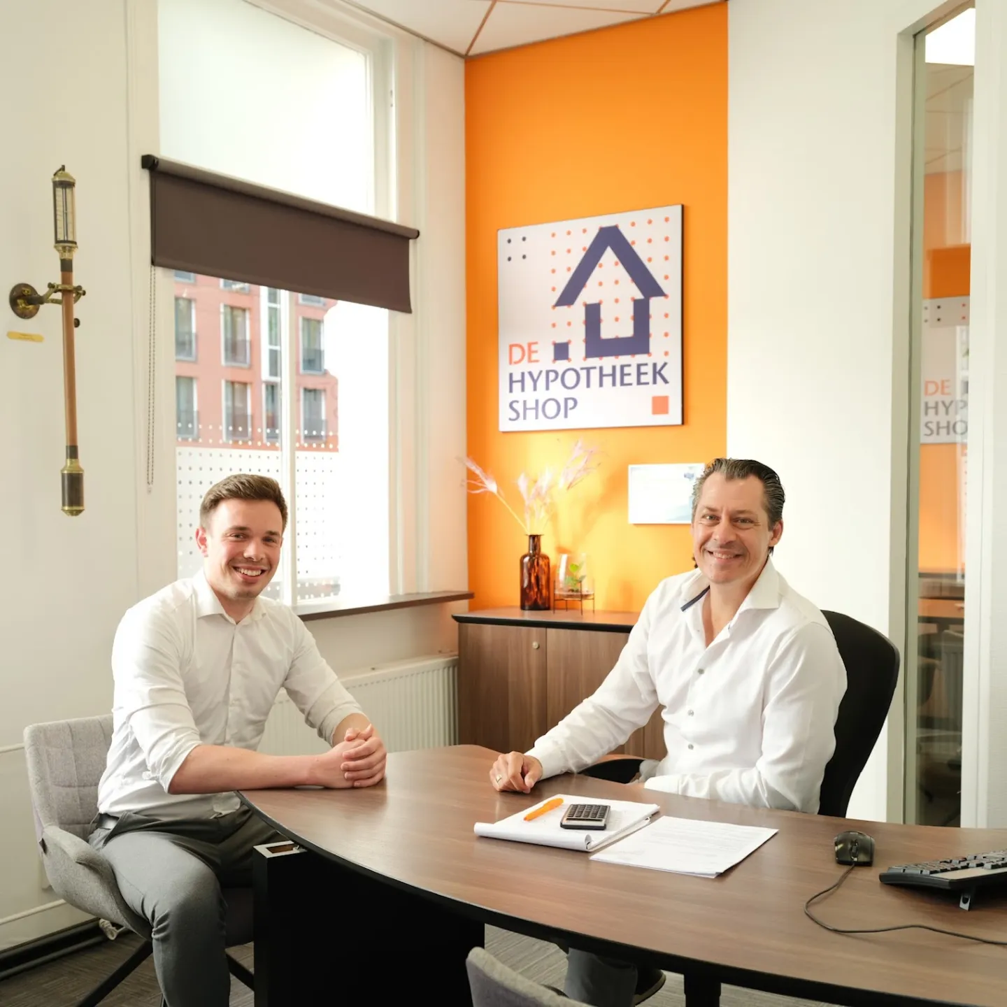 Twee hypotheekadviseurs van Ceintuurbaan zitten samen aan tafel in een kantoor, met documenten en een rekenmachine op het bureau.