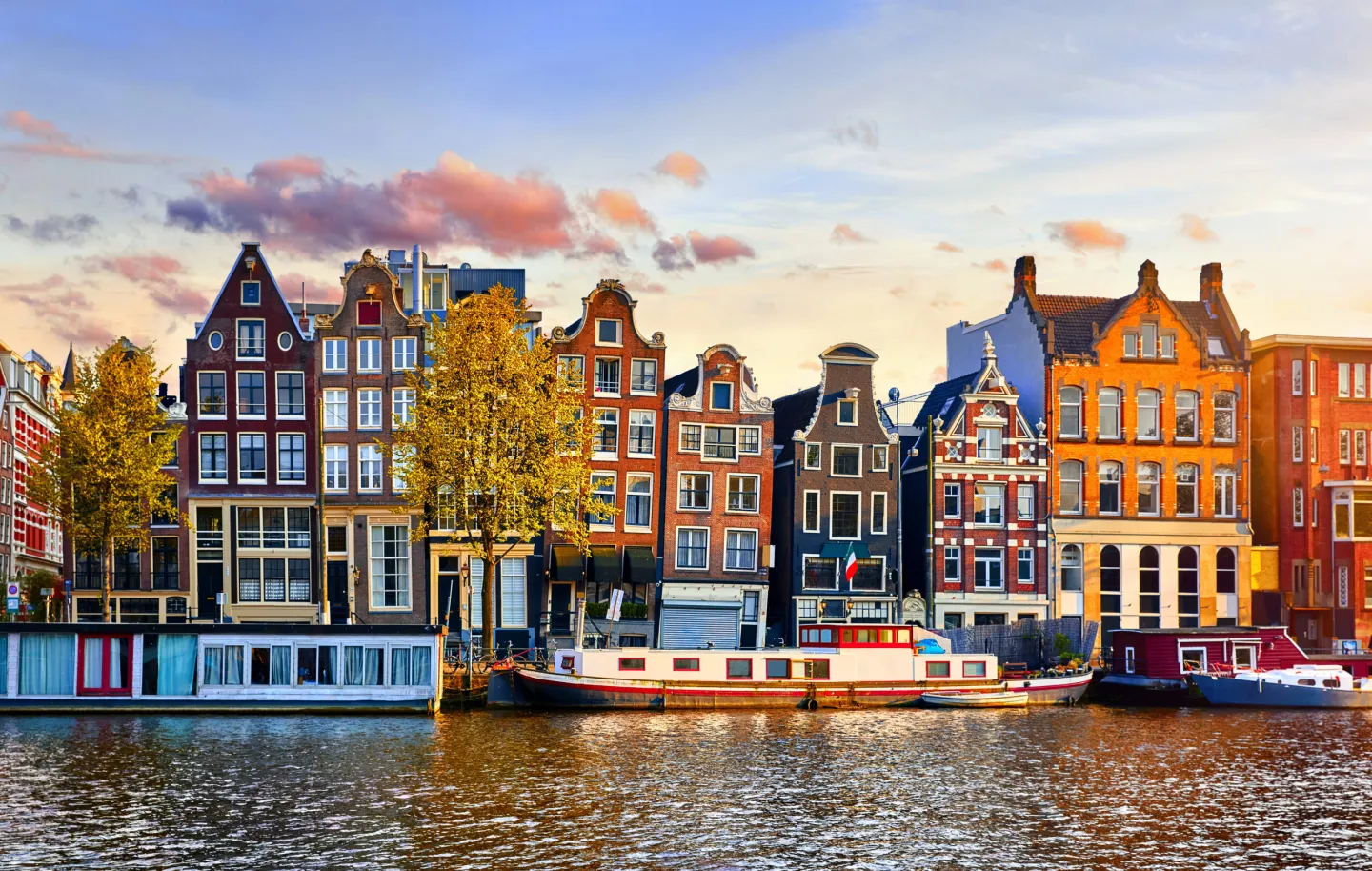 Traditional Amsterdam canal houses and houseboats along the waterfront at sunset.